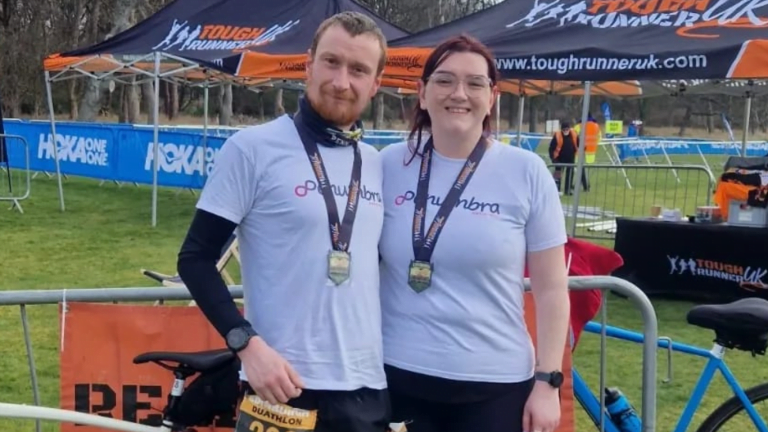 Image shows Cha and Callum smiling to camera in their running gear with their medals
