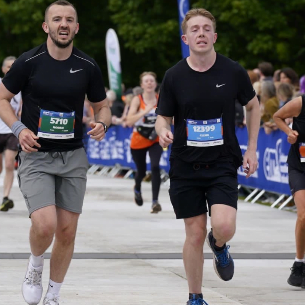 2 Image shows Robbie and Glenn running during the Edinburgh marathon. They're running beside each other wearing a mix of black and grey running shorts and t-shirts.